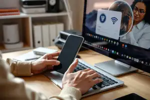 Osoba korzystająca z laptopa i smartfona przy biurku z routerem Wi-Fi, ilustrująca użycie VPN